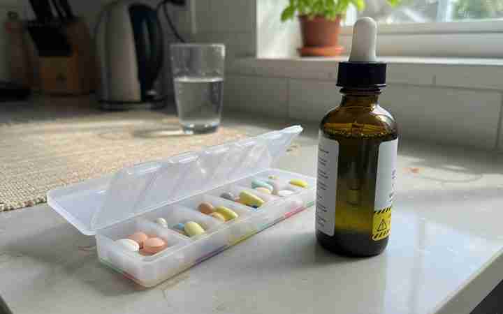 Weekly pill organizer beside an amber CBD tincture and a glass of water